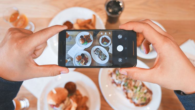 Hands photographing a table of restaurant dishes with a smartphone for social media